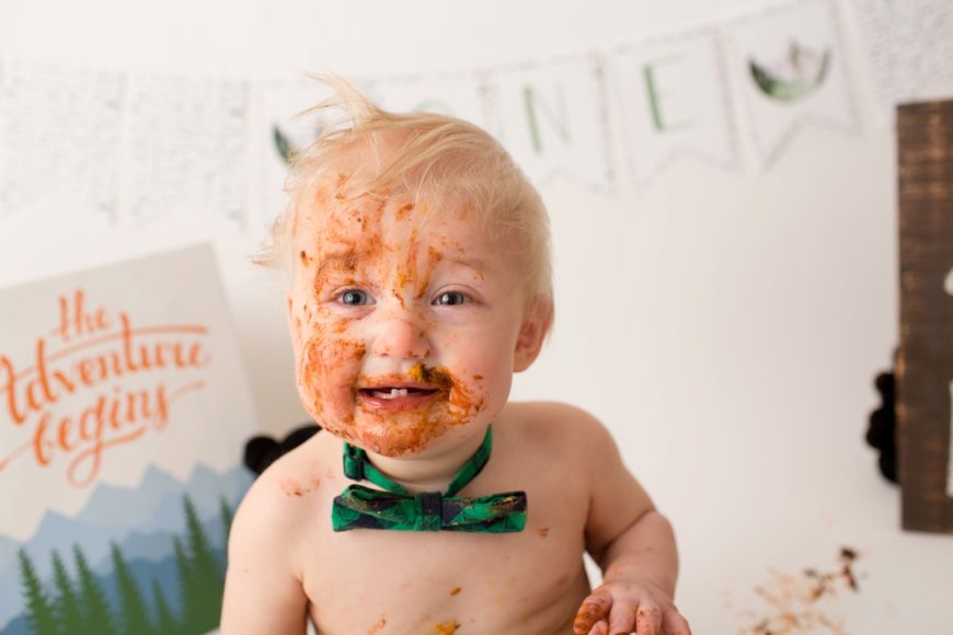 Joyful baby wearing green bowtie during messy cake smash photo session.