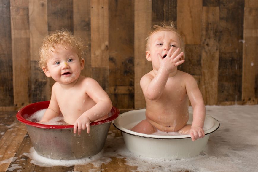 Two babies playing and laughing while sitting in vintage metal wash basins.