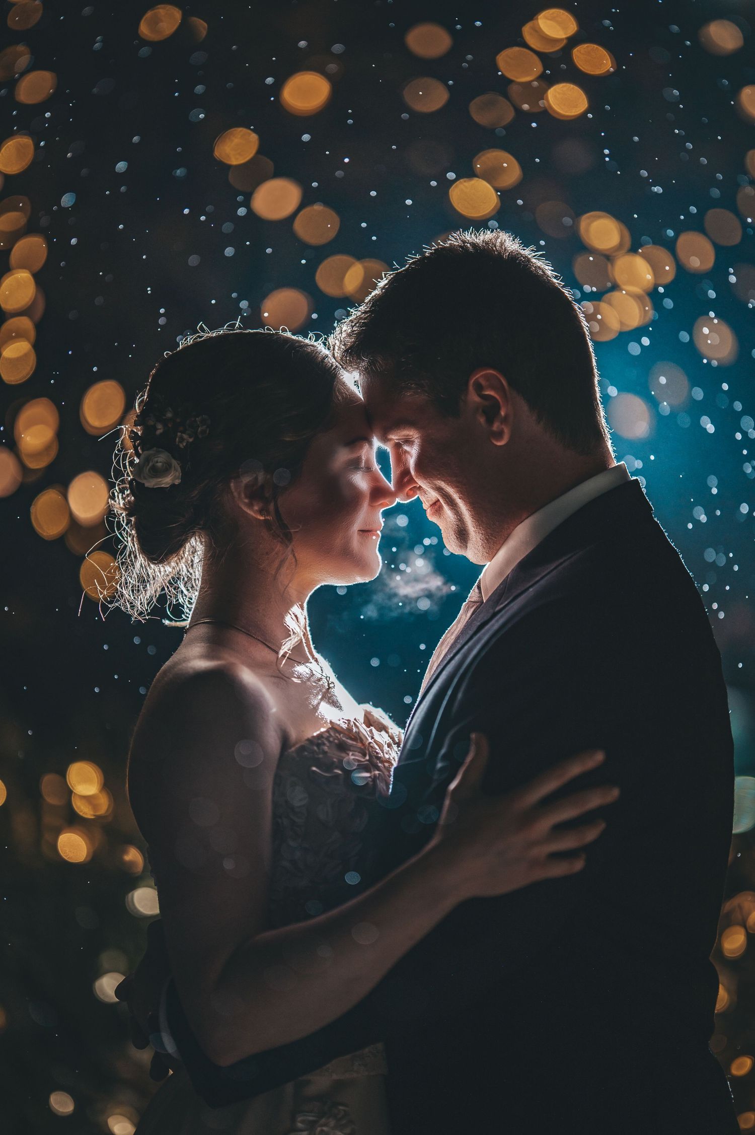 Silhouetted couple embracing against bokeh lights and blue background.
