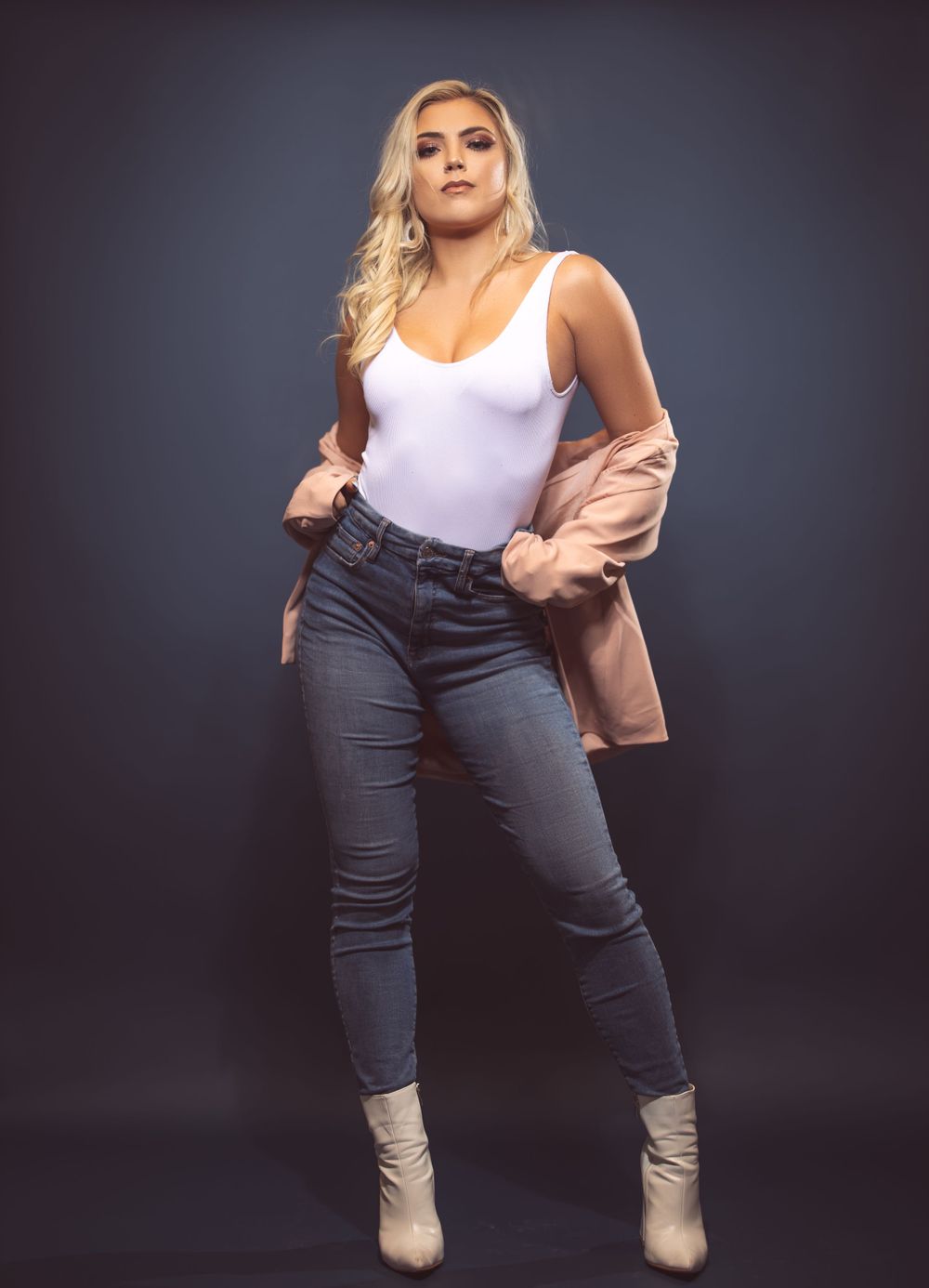 Stylish portrait featuring white bodysuit, pink jacket, and jeans with ankle boots.