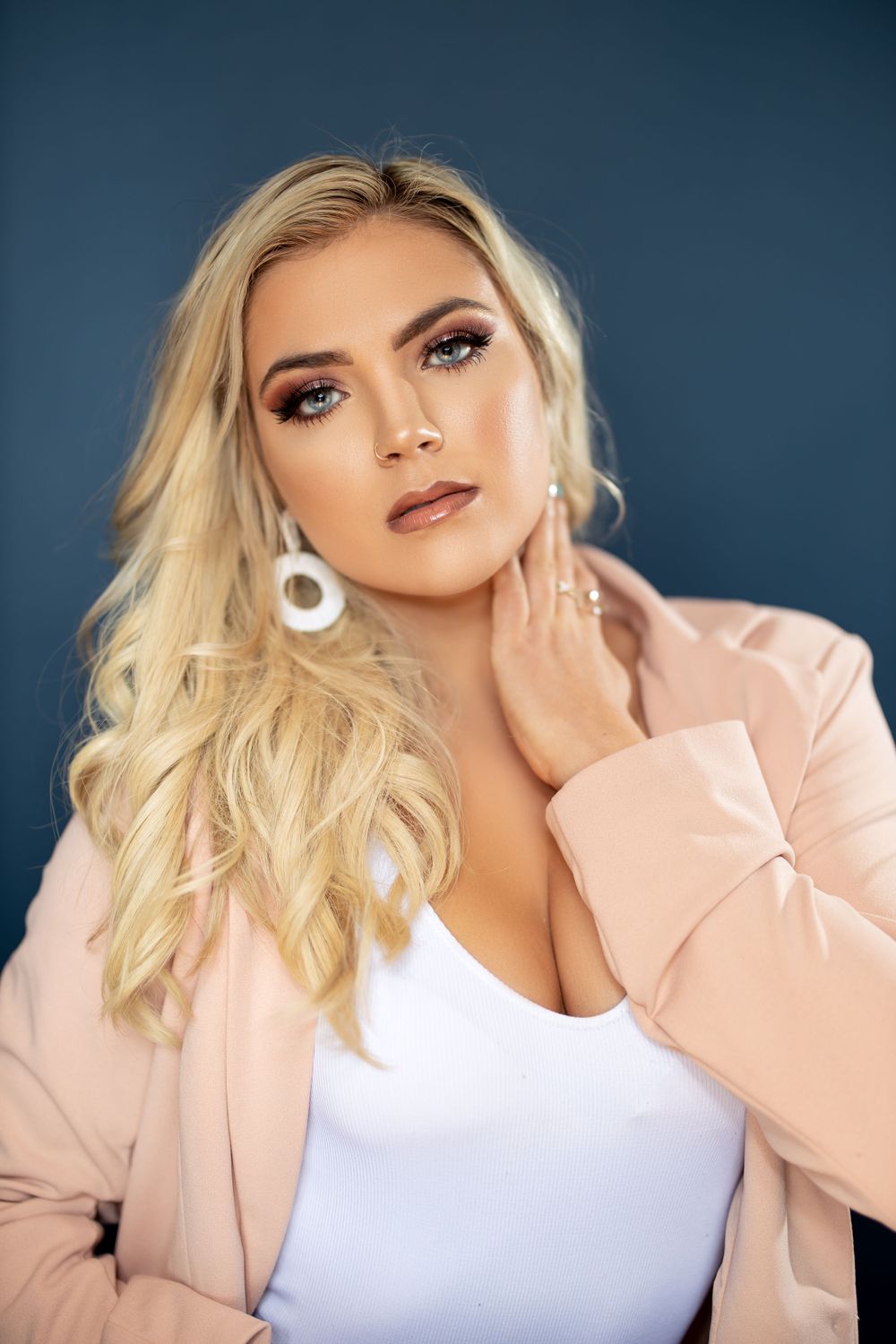 Close-up fashion photo showing glamorous makeup and pink blazer against blue backdrop.