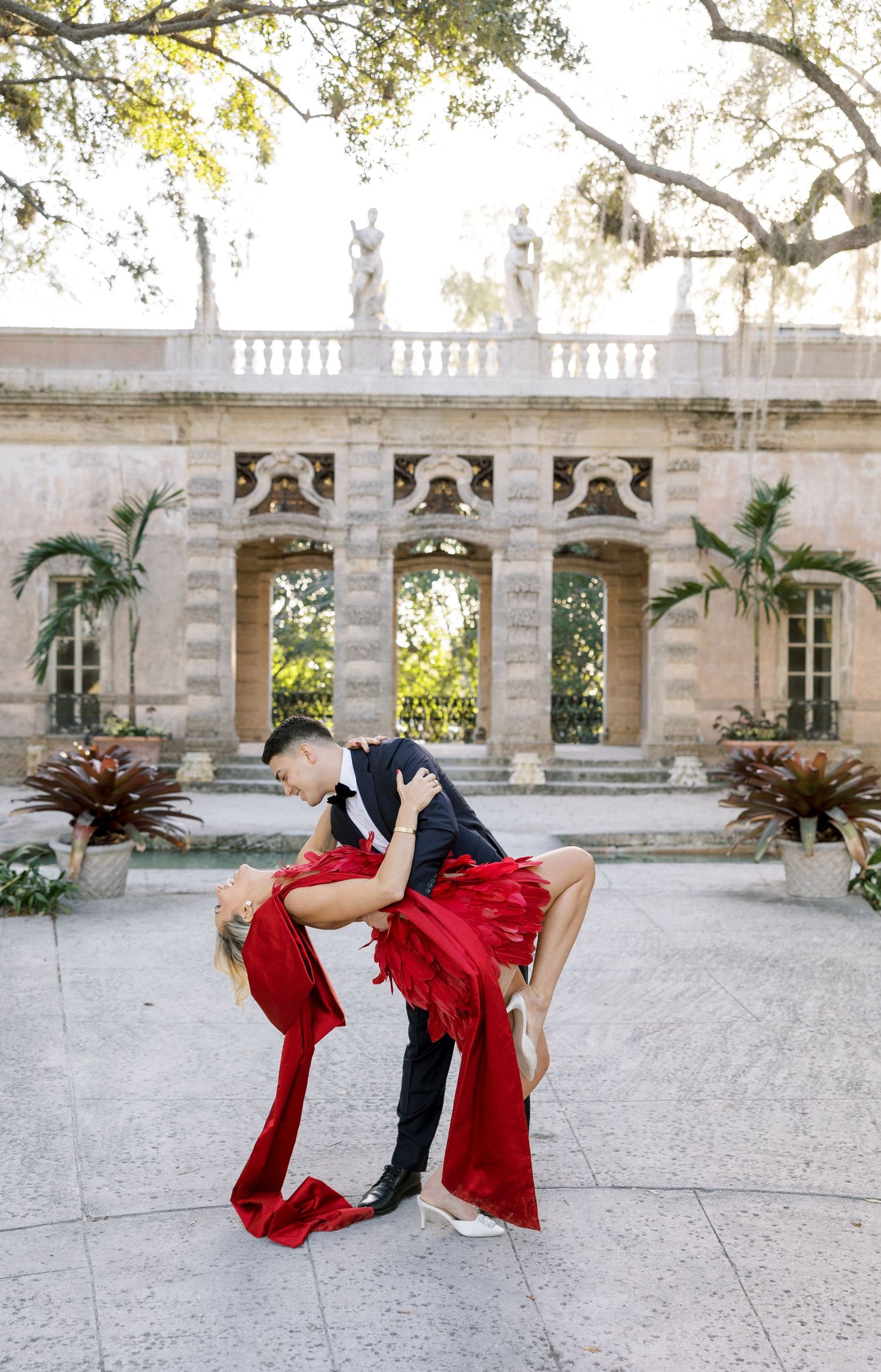 A dramatic dance dip pose performed in front of a classical stone building with palm trees.