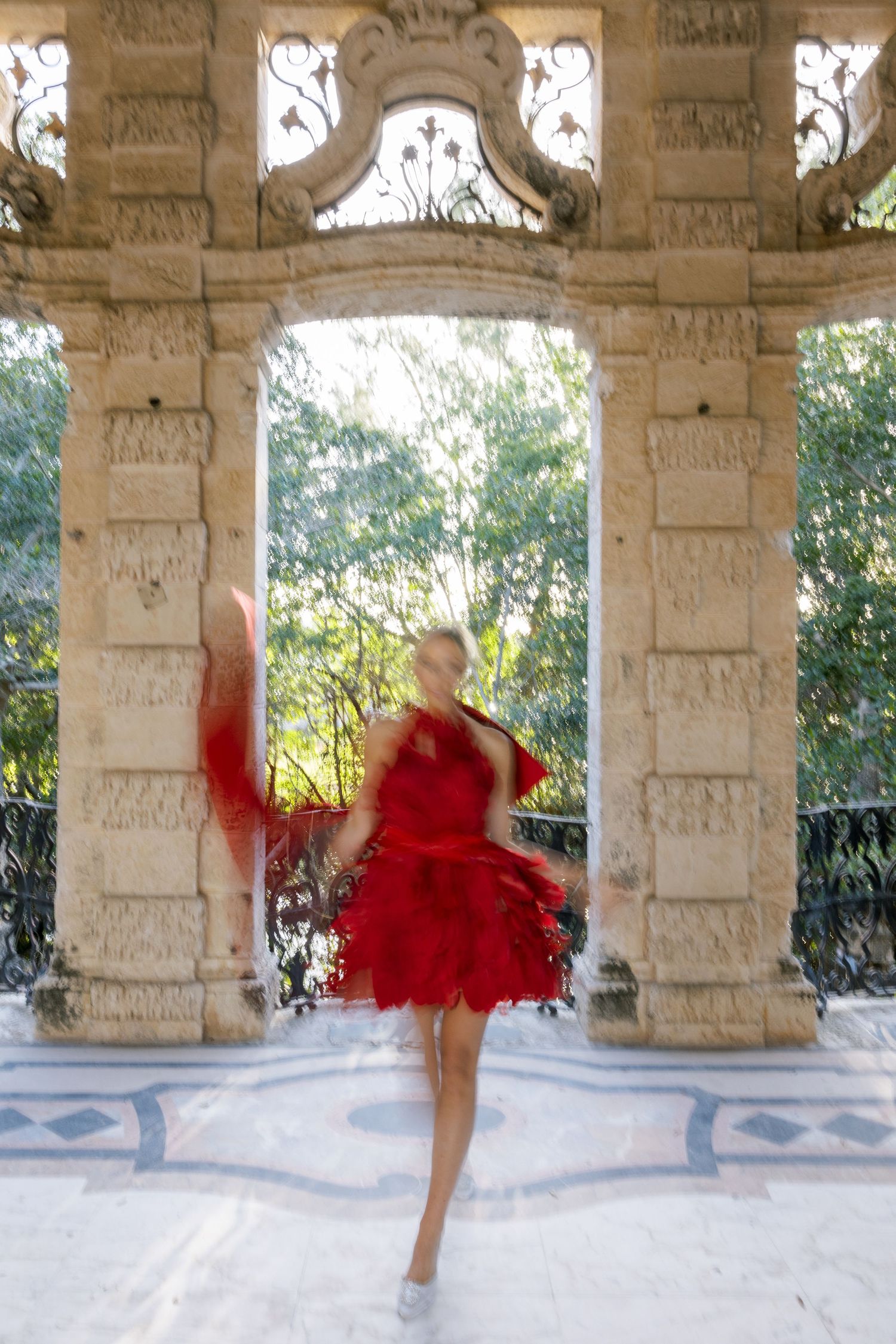 A figure in red spins gracefully in motion beneath an ornate stone colonnade.