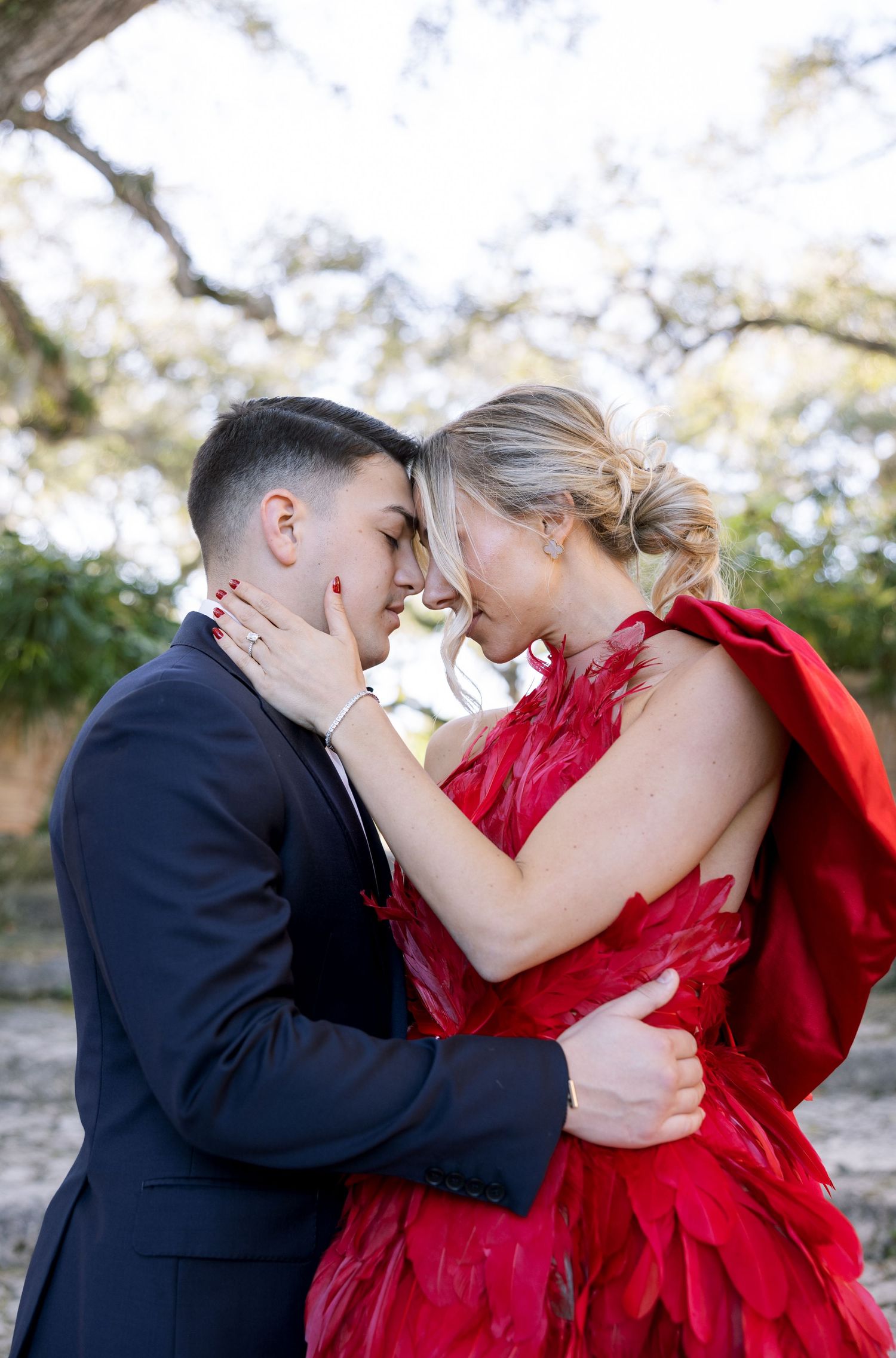 A couple shares an intimate embrace outdoors, with the woman wearing a flowing red dress.