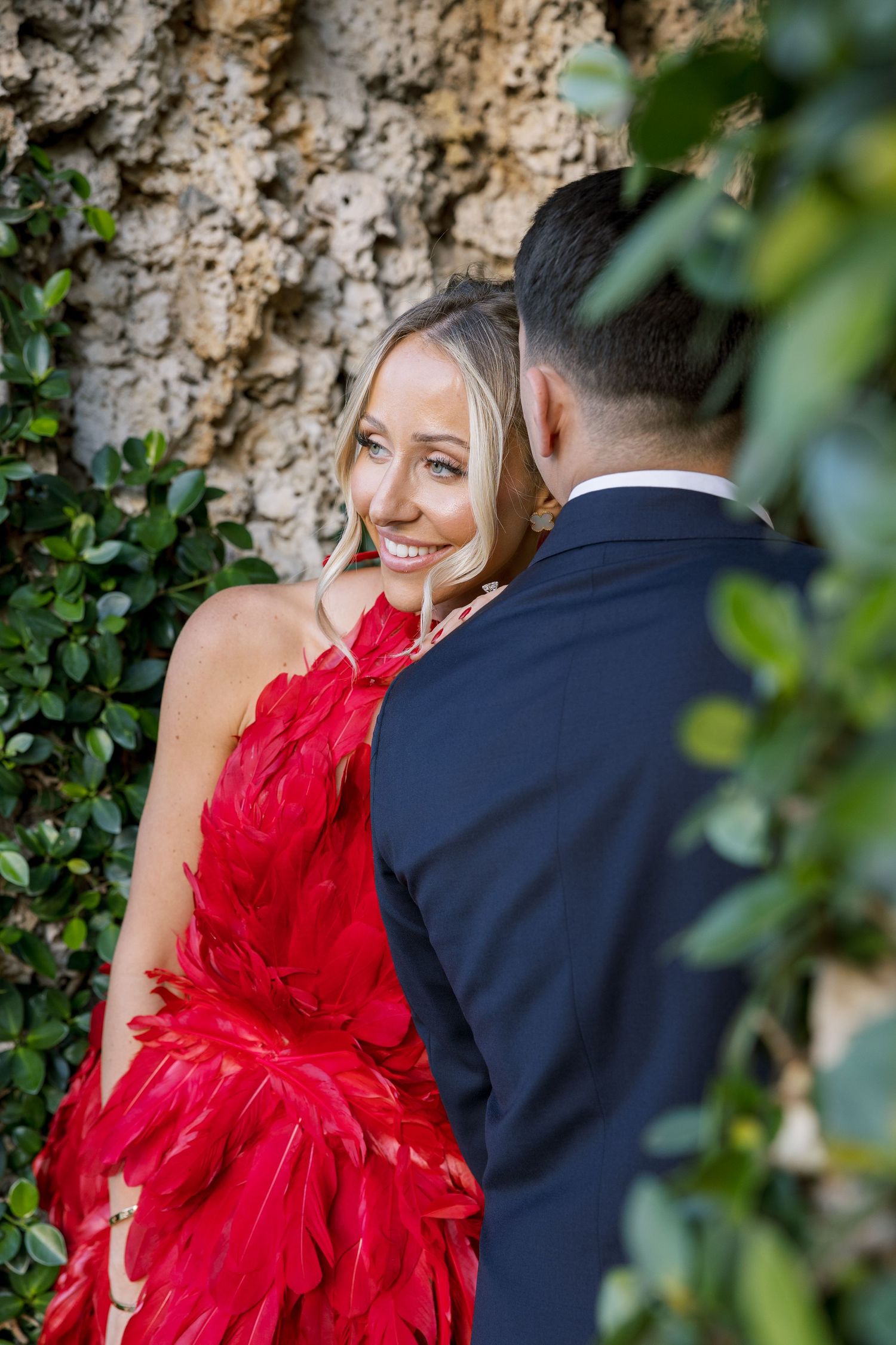 A couple shares an intimate moment against a textured stone wall background.
