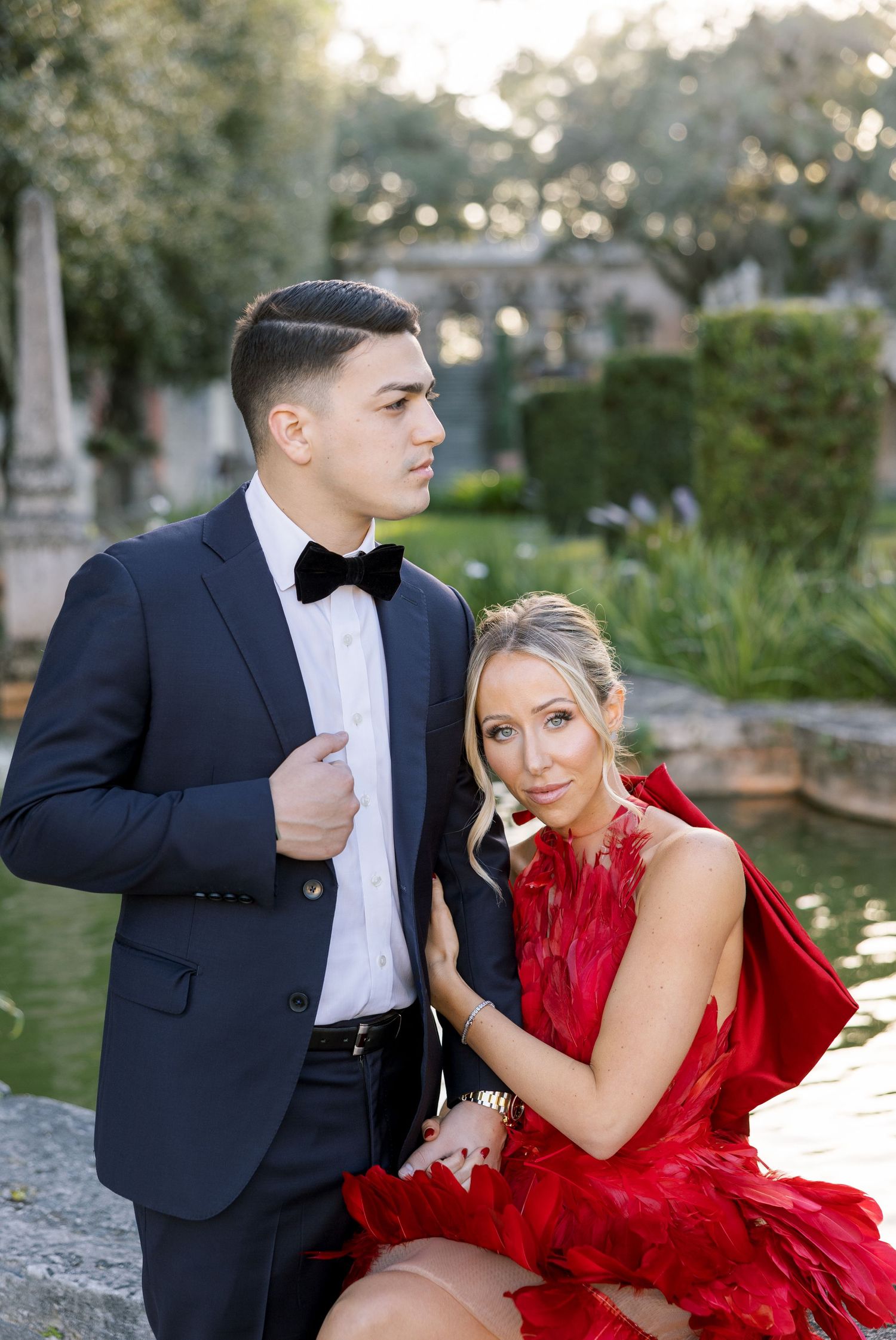 A couple in formal attire pose together in a lush garden setting.