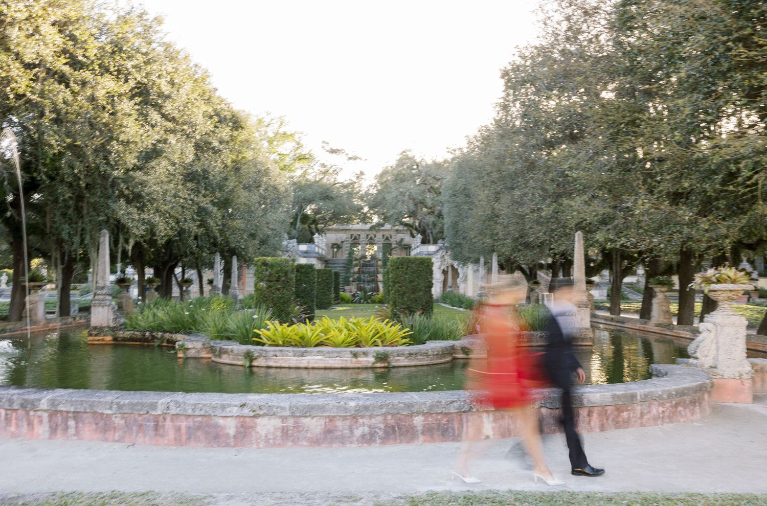 A motion-blurred couple dances through a romantic garden setting with fountains and pathways.