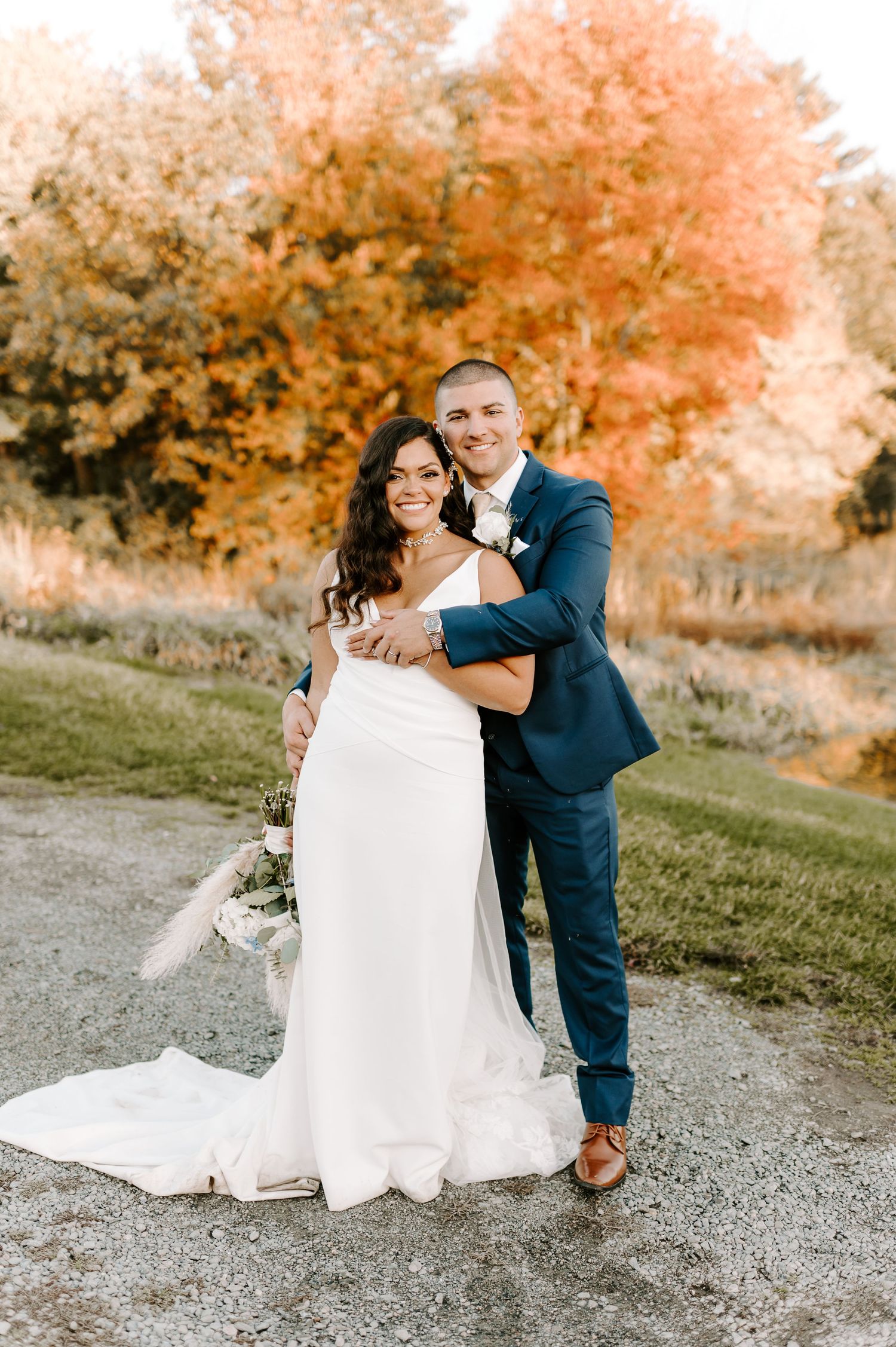 Wedding couple posing against autumn trees with vibrant orange foliage.