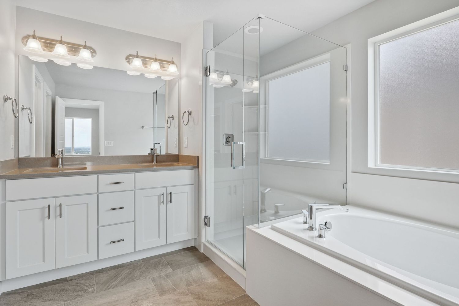 Bright master bathroom with white double vanity, glass shower, soaking tub, and large windows.