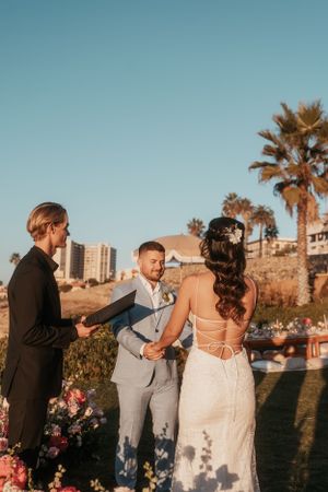 An intimate outdoor wedding ceremony takes place with palm trees and ocean views.