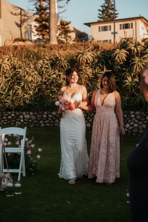 Two people walk on grass during a sunset wedding ceremony surrounded by tropical plants and palm trees.