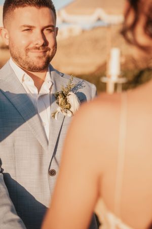 Close-up of a groom in a light blue suit with boutonniere during an outdoor ceremony.