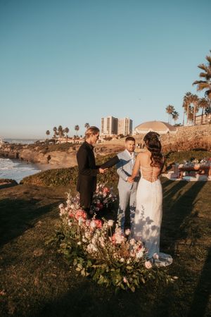 A seaside wedding ceremony with floral arrangements and palm trees against a coastal backdrop.