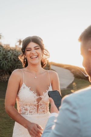 Joyful bride laughing during sunset wedding ceremony.