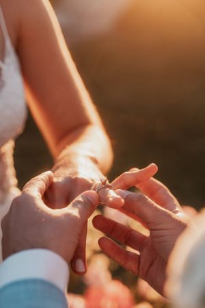 Close-up of wedding ring exchange during outdoor ceremony at golden hour.