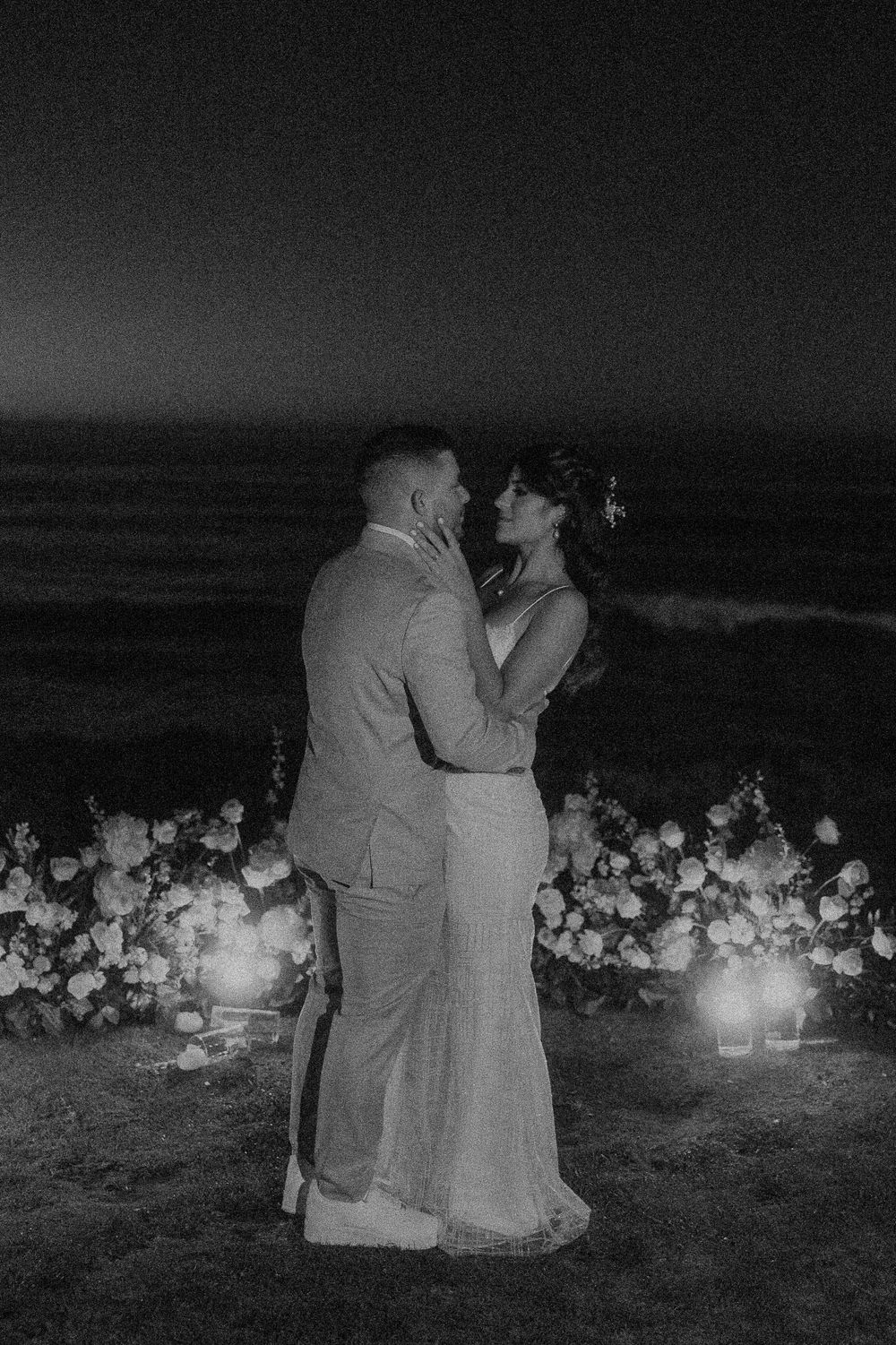 A romantic oceanside wedding scene with floral decorations and candlelight at night.