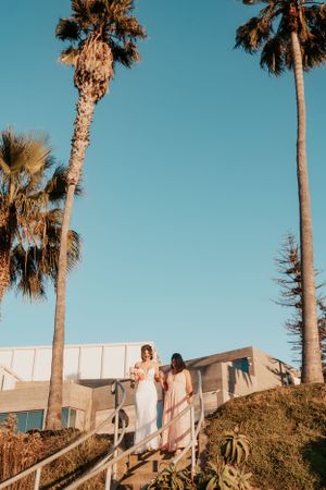 A wedding ceremony setup on a hill with tall palm trees and modern architecture in the background at sunset.