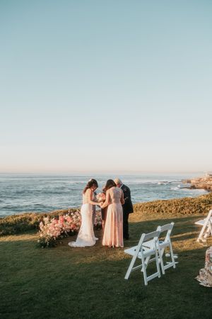 Oceanfront wedding ceremony with white chairs and pink floral arrangements at sunset.