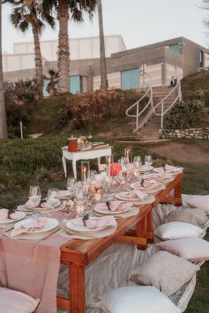 Long rustic wooden table set for an elegant outdoor reception with pink linens and place settings.
