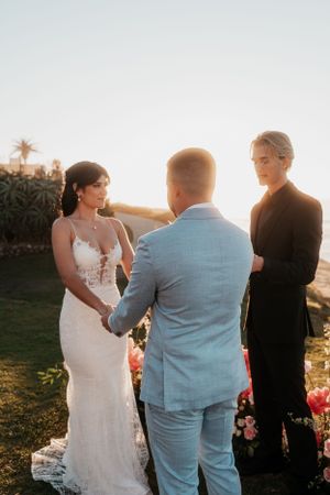 An intimate wedding ceremony takes place on a grassy cliff overlooking the ocean at sunset.