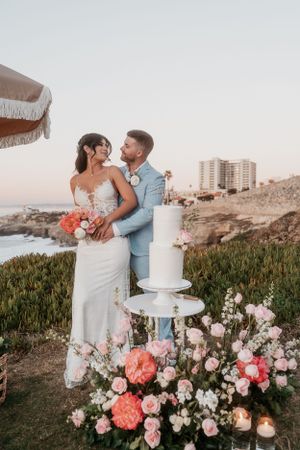 Wedding cake display surrounded by lush floral arrangements and candles with ocean view.