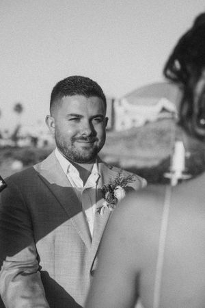 Black and white portrait of a groom wearing a light colored suit and boutonniere on his wedding day.