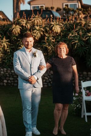 Wedding guests gather on a lawn with palm trees at sunset.