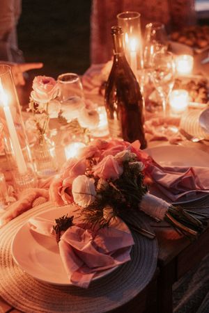 Romantic candlelit table setting with wine bottle and floral arrangements.