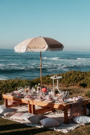 Beachside wedding reception setup with umbrella-shaded tables overlooking the ocean.