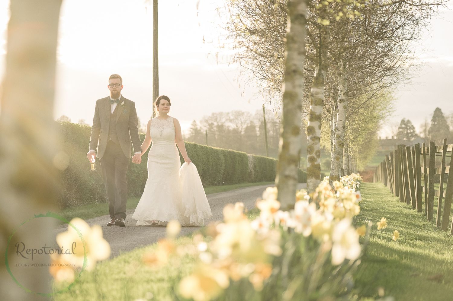 Reportage detail shot of wedding couple walking along drive in spring time with sun flare and daffodils