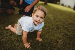 Young child crawling and smiling on green grass during outdoor photoshoot.