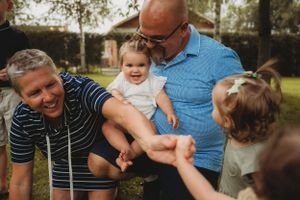 Playful family interaction with toddler outdoors on grass.