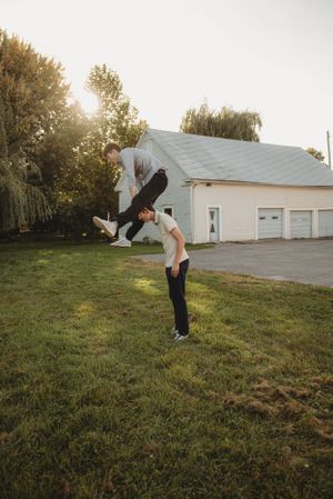 Playful outdoor photo of people doing acrobatic lifts in front of a white garage.