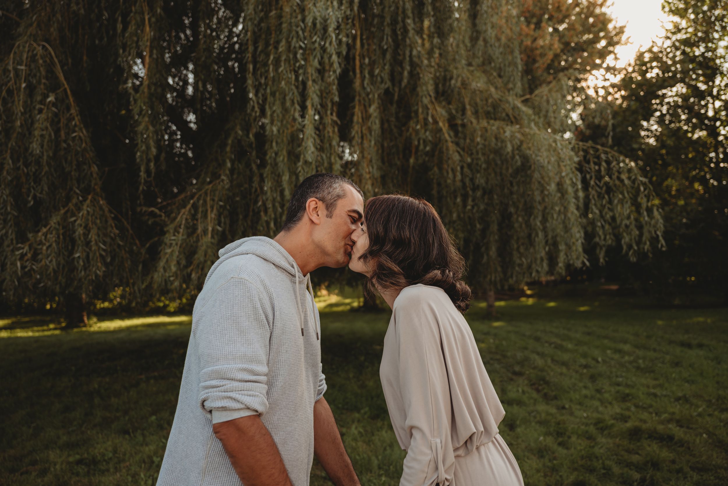A romantic moment captured between two people under a weeping willow at sunset.