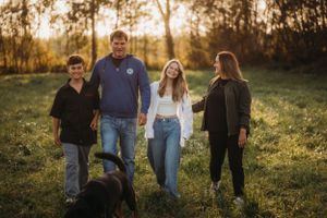 A family group stands together in a grassy field with golden sunset light filtering through trees.