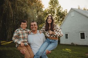 Family group sitting together and smiling outside white building during sunset.