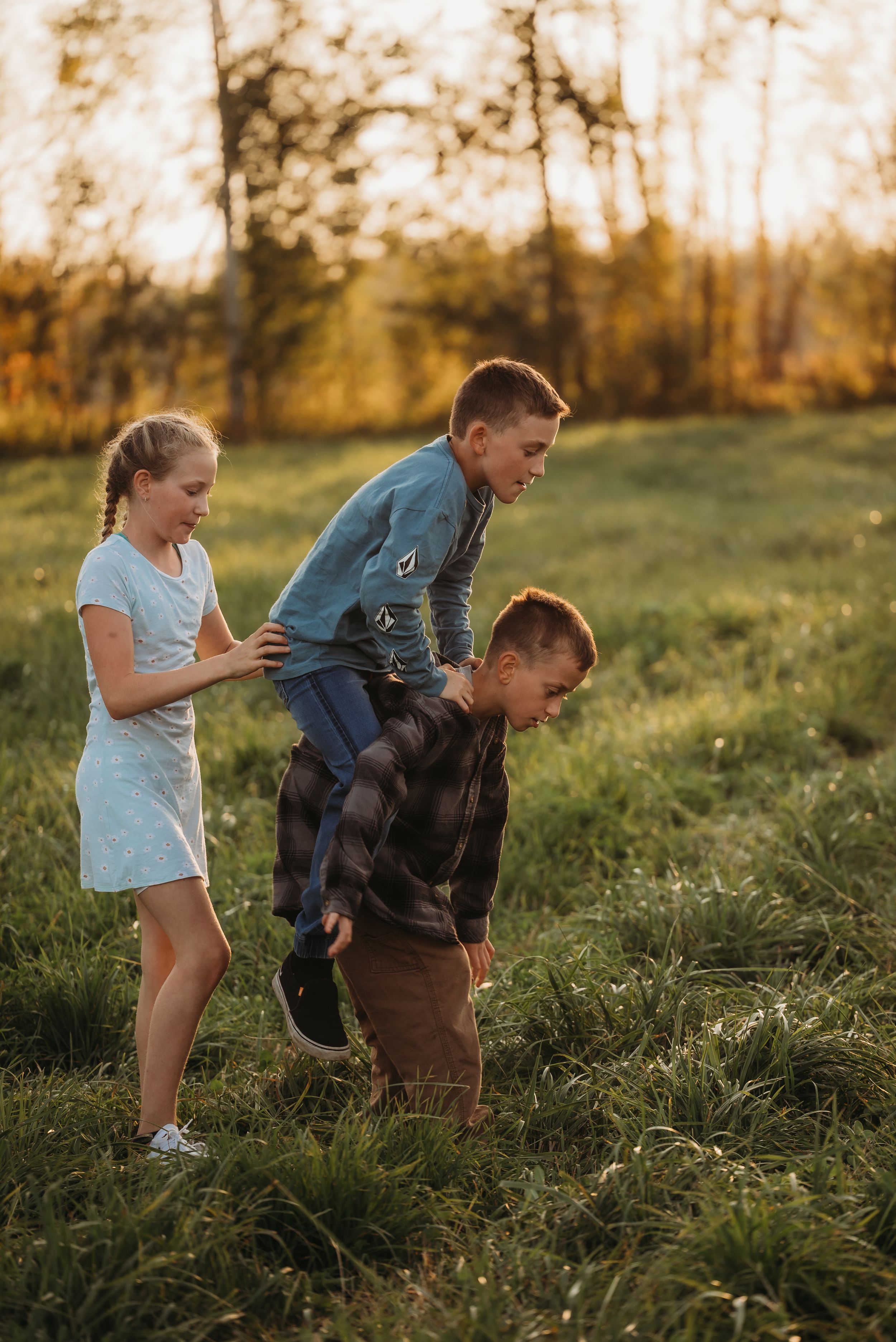 Children playing and climbing on each other in a sunny field during golden hour.