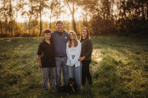 A family of four poses together with their dog in a sunlit field during autumn.