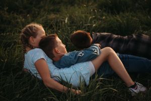 Children laying in tall grass during sunset enjoying playful moment together.