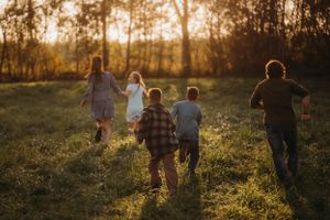 Running together through a grassy field at sunset with trees silhouetted in background.