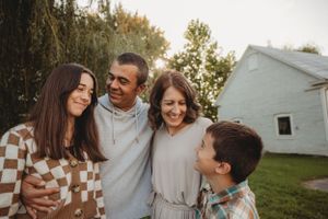 A family of four shares a candid moment together outdoors near a white house.