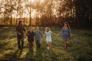 People holding hands while running through tall grass during golden hour.