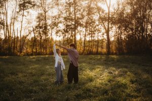 A couple dances together in a sunlit meadow during golden hour.