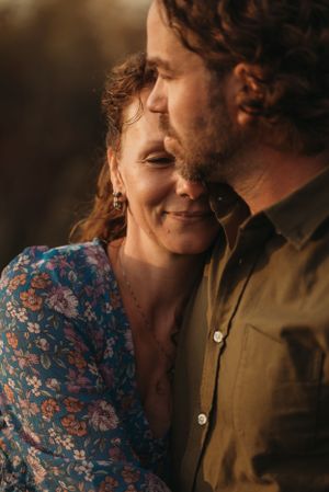 A romantic couple shares an intimate moment in golden sunlight while smiling.