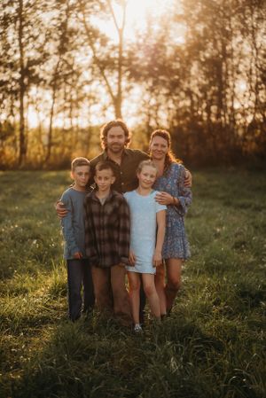 Family standing close together in a sunlit field with forest backdrop.