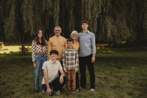 A small family group poses together in front of a dramatic weeping willow tree.