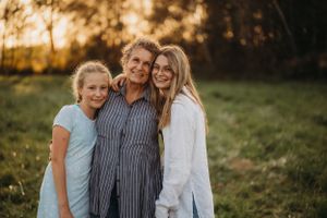 Three people share a warm embrace while standing in a sun-dappled field.