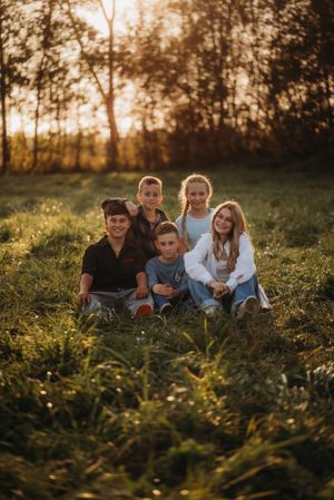 Family portrait in a golden meadow with sunset lighting filtering through trees in background.