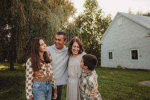 A family group laughs together while posing outdoors near a white building.