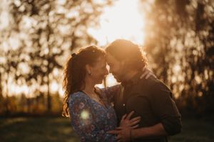 Couple embracing in warm sunset light with lens flare and forest background.